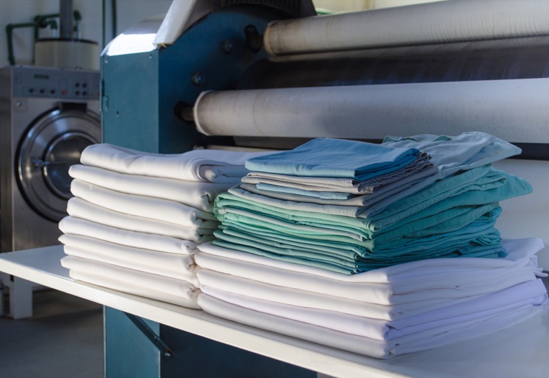 Stack of folded clean sheets or fabrics and industrial iron in an industrial laundry. 