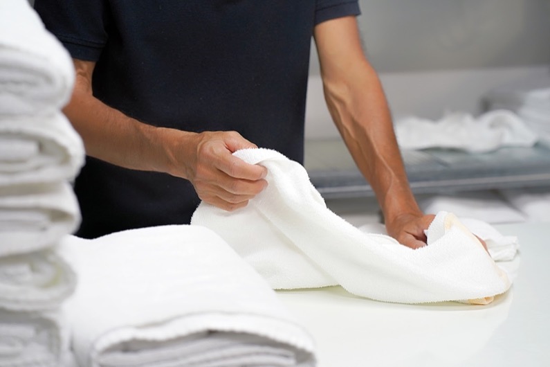 Hands of caucasian male laundry hotel worker folds a clean white towel. Hotel staff workers. Hotel linen cleaning services.