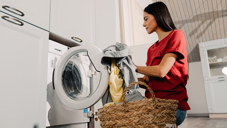Young hispanic woman putting clothes at washing machine