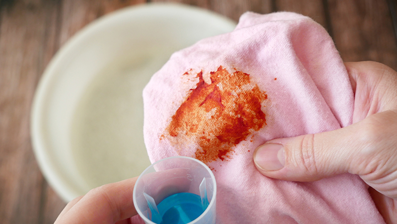 Women's hands in gloves washing dirty stained on colored cloth with a stain remover and soak in soapy water