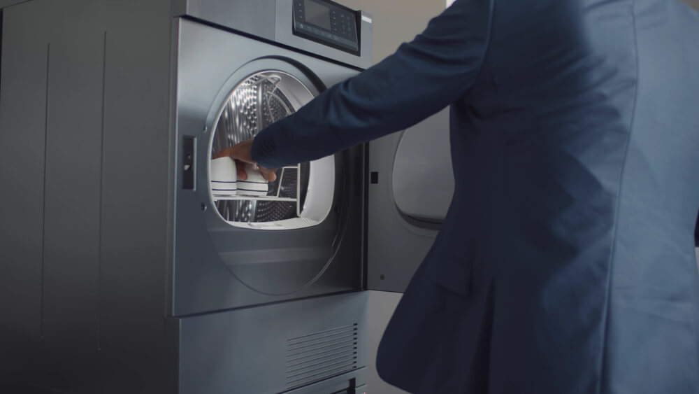 Businessman in suit open modern cloth dryer taking clean shoes. Cropped shot of elegant man at home taking dried pair of shoes from washing machine. Modern technology concept
