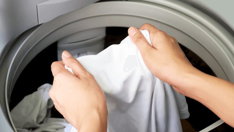 Woman hand taking wet white clothes out of automatic washing machine