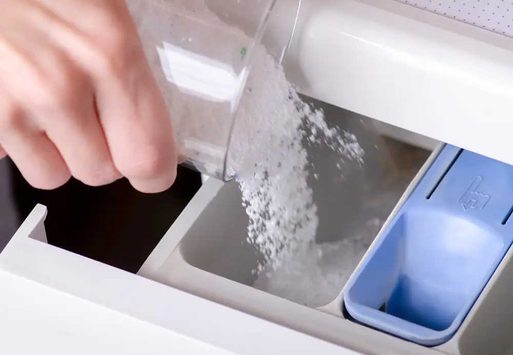 close up of a hand pouring detergent into the washing machine container household