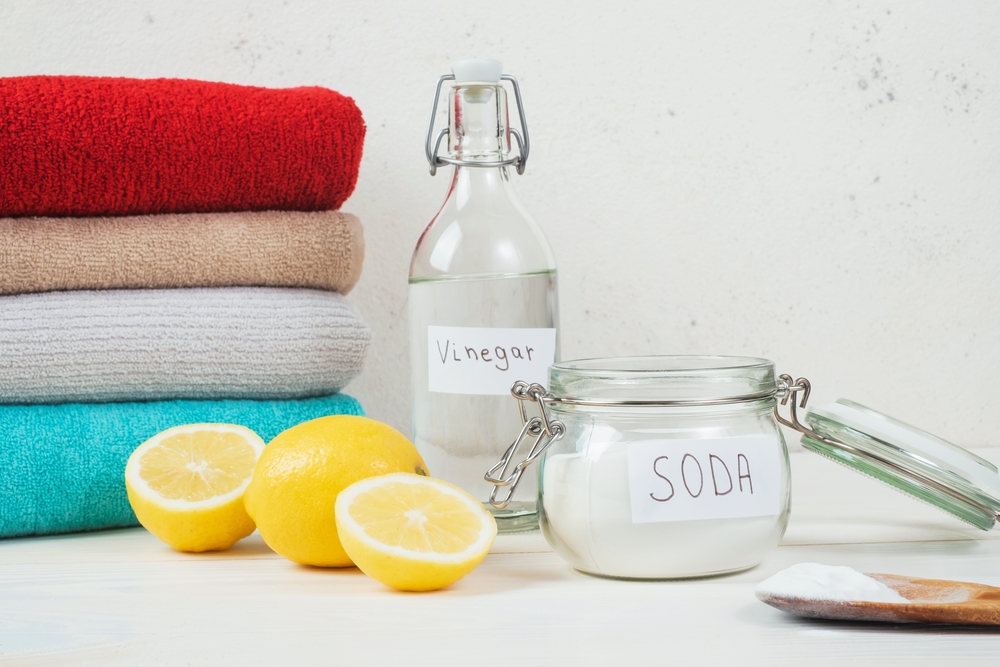 Baking soda in jar, vinegar, cut lemon, folded towel on a white background.